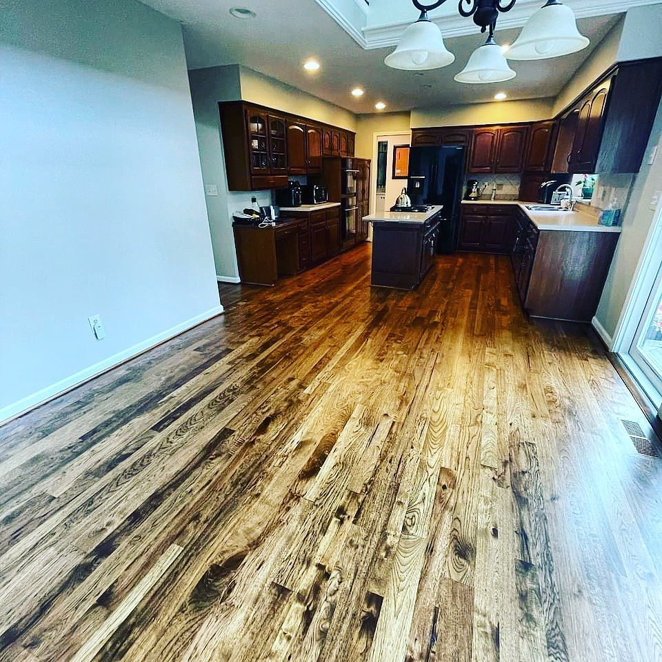 Open-plan kitchen space in Philadelphia showcasing the results of the twelfth hardwood floor refinishing project with rich, dark-stained wood flooring contrasting beautifully against classic wooden cabinetry and modern appliances.